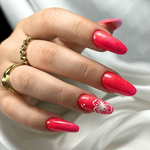 unghie corallo glitterate con fiore bianco